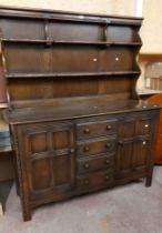 A 1.45m vintage Ercol dark elm two part dresser with two shelf open plate rack over a base with four