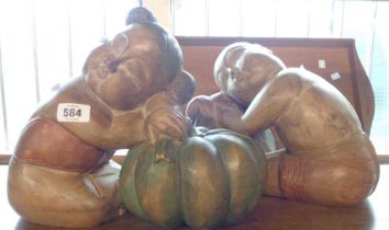 A pair of modern painted carved wood figurines, depicting a boy and girl using pumpkins as pillows