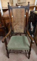 An old oak framed high back elbow chair with remains of rattan panel, open armrests and green