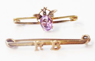 Two unmarked yellow metal bar brooches, one with 'RB' initials, the other set with an amethyst and