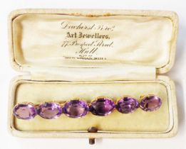 A yellow metal bar brooch, set with six inline oval amethysts - in associated box