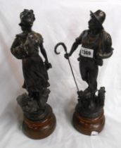 A pair of spelter figures depicting a shepherd and shepherdess set on turned wooden plinths