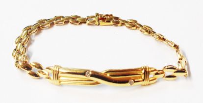 A marked K18 yellow metal bracelet, set with two tiny diamonds to cast central cross-over panel