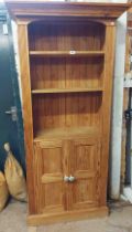 An 87cm modern pine three shelf open bookcase with double cupboard under, set on plinth base