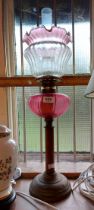 A Victorian oil lamp with brass base, wooden column and cranberry glass reservoir, with chimney