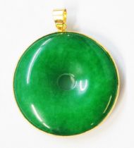 A 3.5cm diameter Chinese yellow metal mounted pendant, set with pierced jadeite disc - in associated