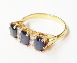 A marked 18ct. yellow metal ring, set with three oval green/dark blue sapphires interspersed with