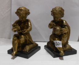 A pair of bronze figurines, each depicting a child in a scholarly pursuit, set on a polished slate