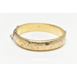 A GOLD PLATED HINGED BANGLE, a hollow gold plated bangle with engraved foliage detail, approximate