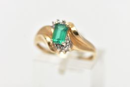 A YELLOW METAL GEM SET RING, designed with a four claw set, rectangular cut emerald, between