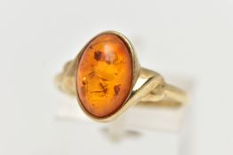 A 9CT YELLOW GOLD AMBER CABOCHON RNIG, collet set with an oval cut amber cabochon, twist detail to