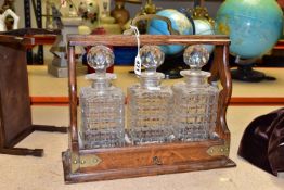 AN EDWARDIAN TANTULUS, with brass mounts, containing three square cut crystal decanters each with