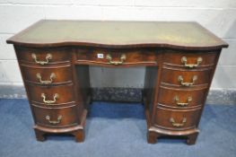 A REPRODUX MAHOGANY SERPENTINE KNEE HOLE DESK, with a green leather writing surface, and nine