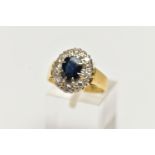 A YELLOW METAL SAPPHIRE AND DIAMOND CLUSTER RING, centering on an oval cut deep blue sapphire, in