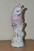 A 20TH CENTURY CONTINENTAL PORCELAIN OWL, decorated in pink and blue, perched on a white tree stump,