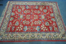 A 20TH CENTURY FLORAL RED GROUND RUG, with a cream multi strap border, 220cm x 172cm (condition:-low