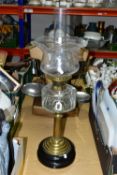 A TALL OIL LAMP, having a glass reservoir supported on a brass column and a black plinth style base,
