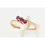 A THREE STONE RUBY RING, three circular cut rubies prong set in yellow metal, leading on to a bypass