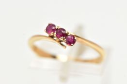 A THREE STONE RUBY RING, three circular cut rubies prong set in yellow metal, leading on to a bypass