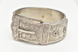 A SILVER HINGED BANGLE, in the form of a belt and buckle, decorated with a floral pattern,