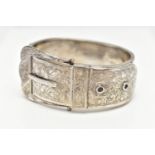 A SILVER HINGED BANGLE, in the form of belt and buckle, decorated with a floral pattern,