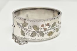 A SILVER HINGED BANGLE, a wide bangle decorated with a yellow and rose metal foliage etched pattern,