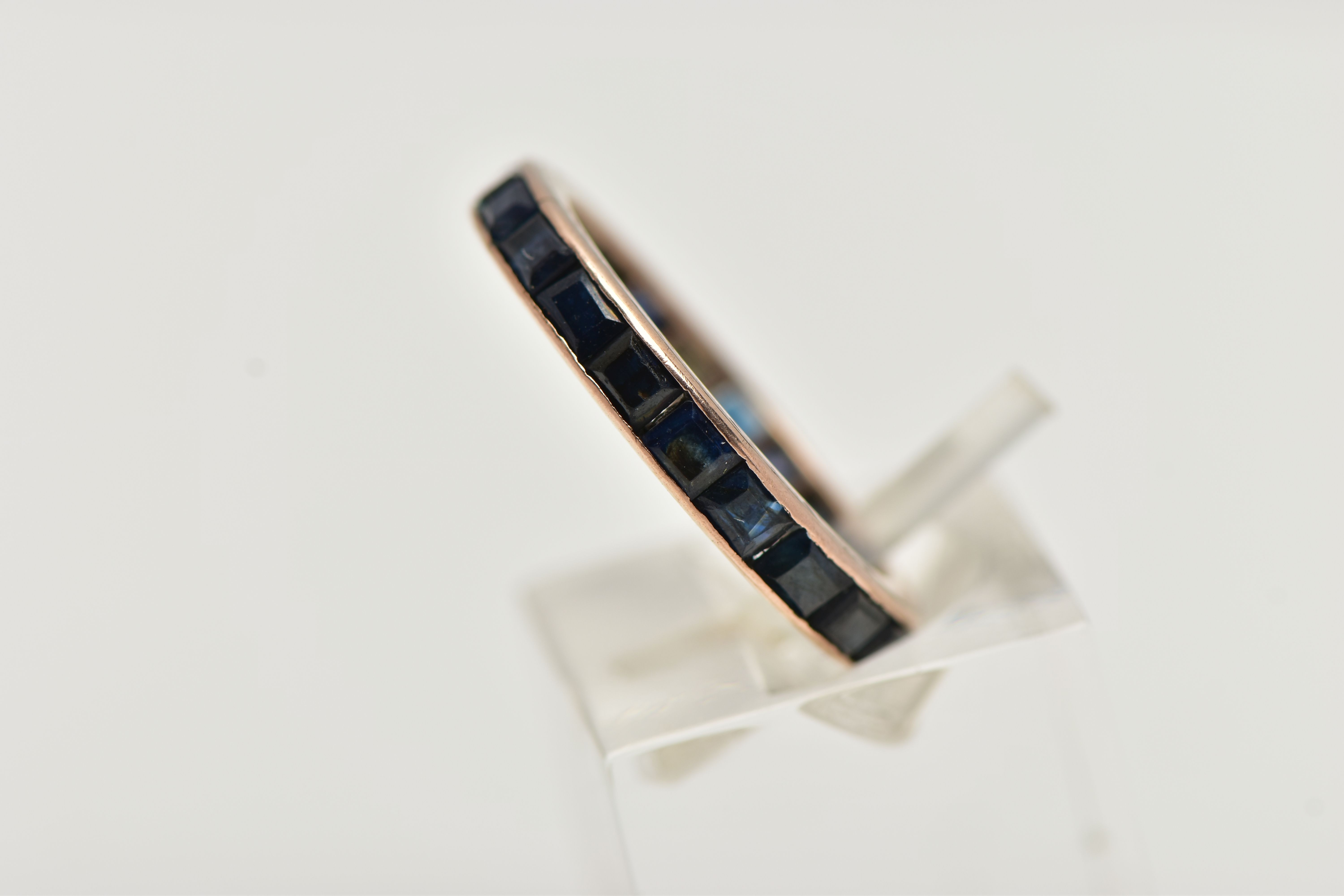 A ROSE METAL FULL ETERNITY RING, set with a full row of square cut deep blue sapphires, channel - Image 2 of 4