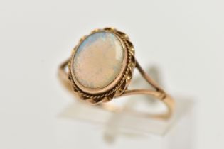 A 9CT GOLD OPAL RING, designed with an opal cabochon, in a milgrain collet setting, to a rope