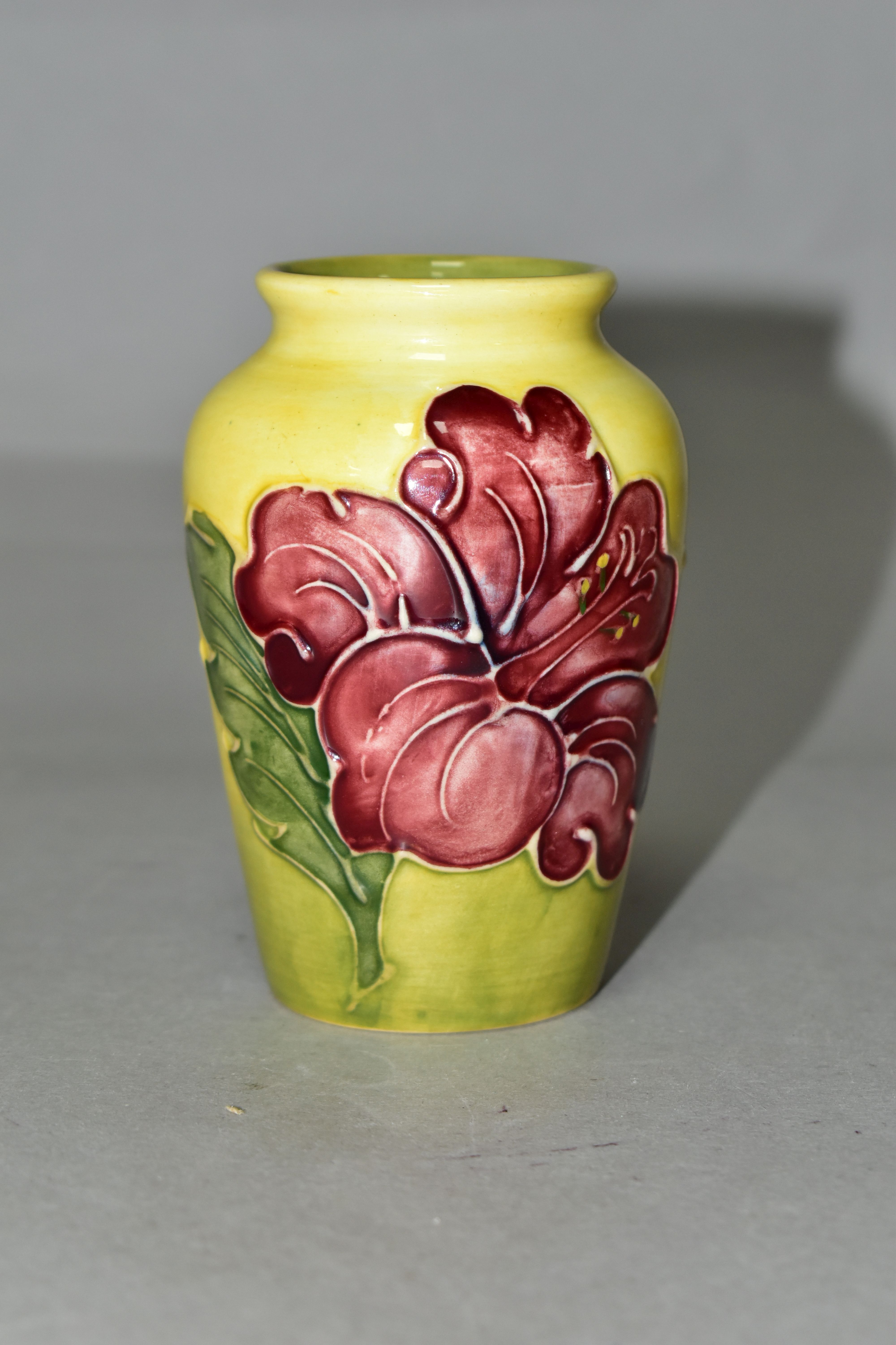 A SMALL MOORCROFT POTTERY HIBISCUS VASE, tube lined with red/purple hibiscus on a graduated yellow