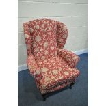 A RED FLORAL PATTERN WING BACK ARMCHAIR, on ebonised cabriole legs (condition:-slightly dirty