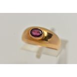 A YELLOW METAL GARNET SET RING, set with an oval cut garnet in a raised collet setting, to a