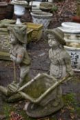 TWO WEATHERED COMPOSITE GARDEN FIGURES, of a boy and girl farming with a wheelbarrow and push