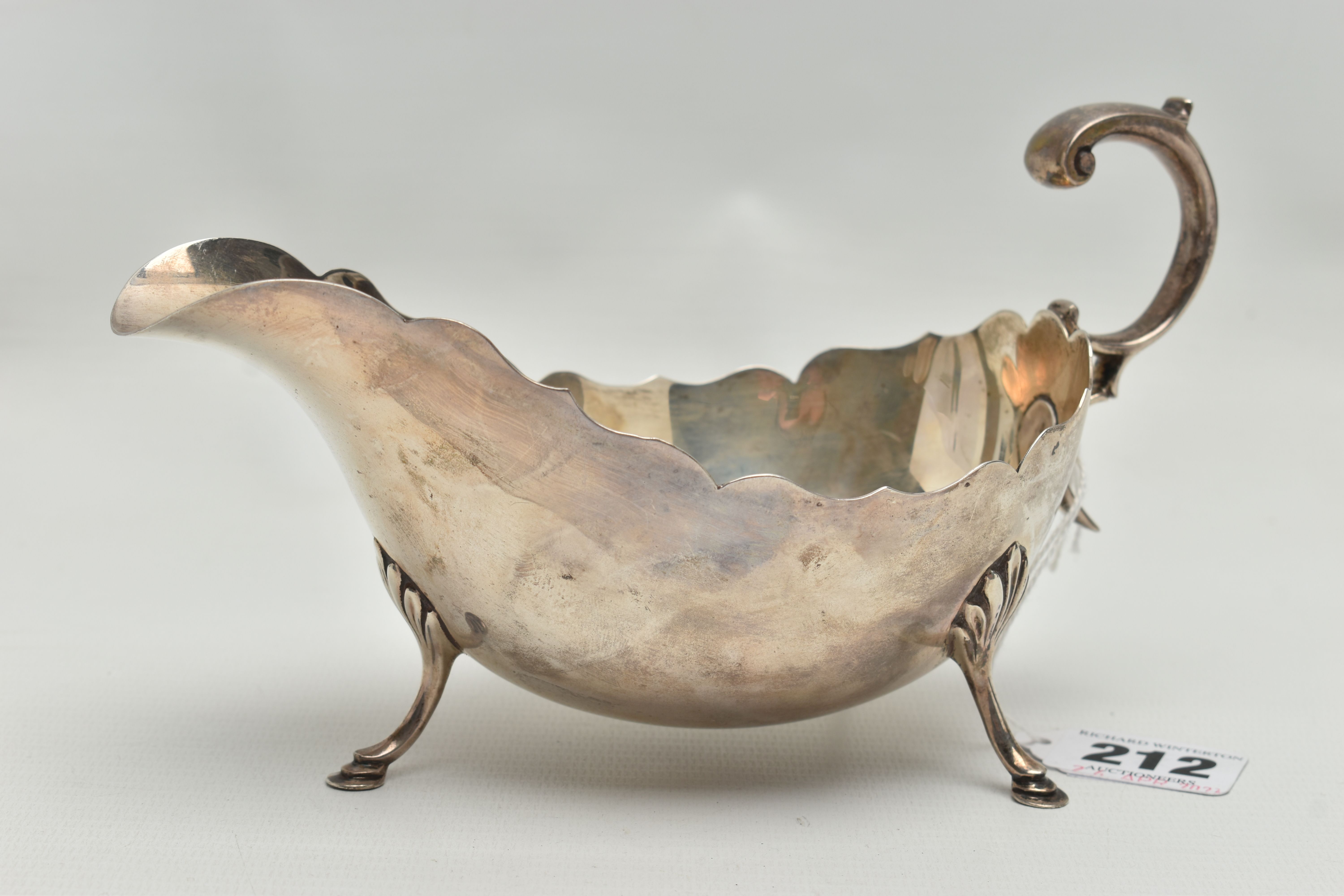 A GEORGE V SILVER SAUCE BOAT WITH WAVY RIM, 'S' scroll handle, on three cabriole legs with shell