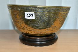 A CHINESE BRASS BOWL, on a wooden stand, the bowl engraved with various creatures, cast character
