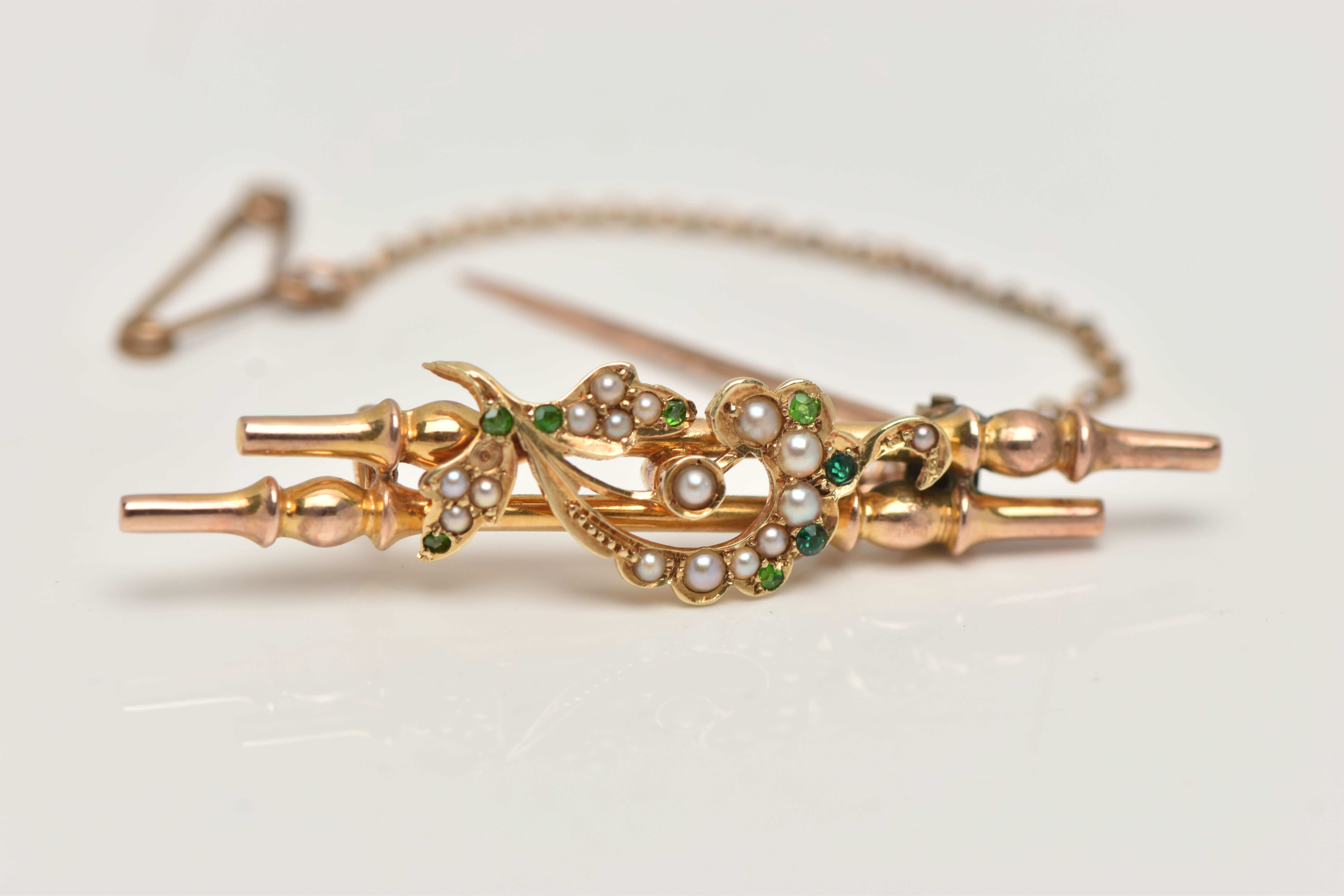 A YELLOW METAL BROOCH, double bar brooch with floral detailing, set with green stones assessed as