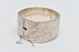 A SILVER HINGED BANGLE, a wide bangle engraved with a floral and foliage design, approximate width