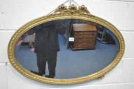 A 19TH CENTURY OVAL GILTWOOD WALL MIRROR, with a floral pediment and bevelled edged plate 84cm x