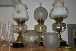 THREE OIL LAMPS AND A SELECTION OF SHADES, the oil lamps all having glass reservoirs - one with