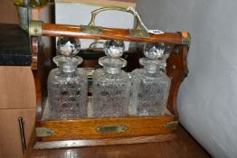 AN EDWARDIAN OAK TANTULUS, with three decanters, original stoppers (one chipped at base), locking