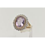 A 9CT GOLD AMETHYST AND DIAMOND DRESS RING, a principal set oval cut amethyst with halo surround