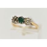 A YELLOW METAL EMERALD AND DIAMOND THREE STONE RING, centring on an oval cut emerald, flanked with