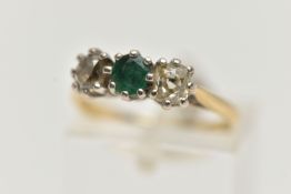 A YELLOW METAL EMERALD AND DIAMOND THREE STONE RING, centring on an oval cut emerald, flanked with