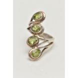 A WHITE METAL PERIDOT DRESS RING, designed with a row of four oval cut peridots each collet set to