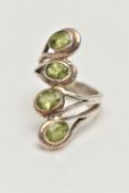 A WHITE METAL PERIDOT DRESS RING, designed with a row of four oval cut peridots each collet set to