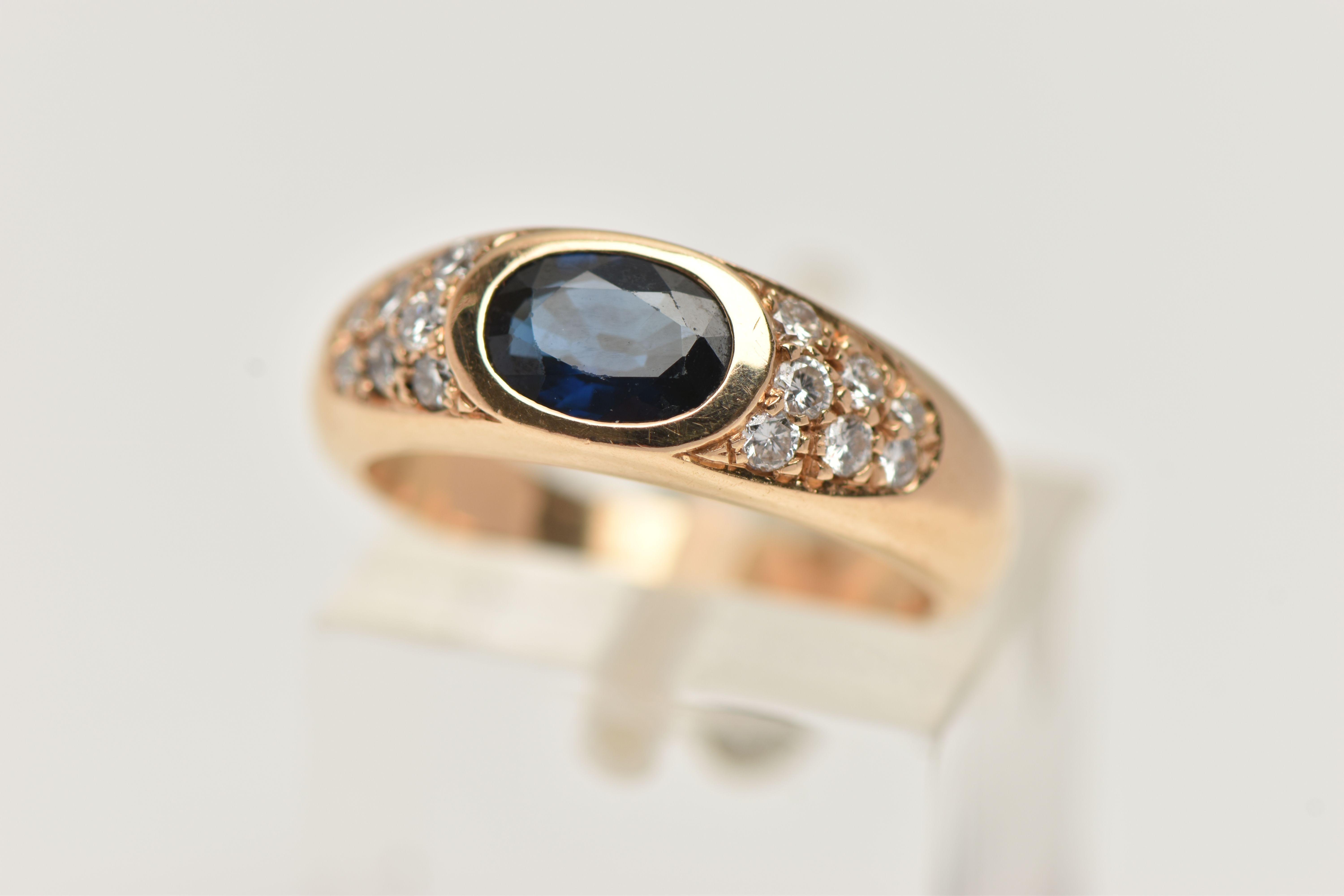 A YELLOW METAL SAPPHIRE AND DIAMOND RING, designed with a central oval cut deep blue sapphire,