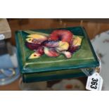 A MOORCROFT POTTERY RECTANGULAR TRINKET BOX AND COVER, green / blue ground, decorated with an orchid