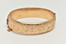 A 9CT GOLD HINGED BANGLE, foliage pattern to one side, fitted with a push piece clasp with