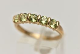 A 9CT GOLD PERIDOT RING, set with a row of five circular cut peridots, each tension set, to a