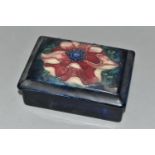 A MOORCROFT POTTERY RECTANGULAR TRINKET BOX AND COVER DECORATED IN A PINK ANEMONE PATTERN, on a dark