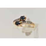 AN 18CT GOLD SAPPHIRE AND DIAMOND RING, cross over design, set with two oval cut blue sapphires, and